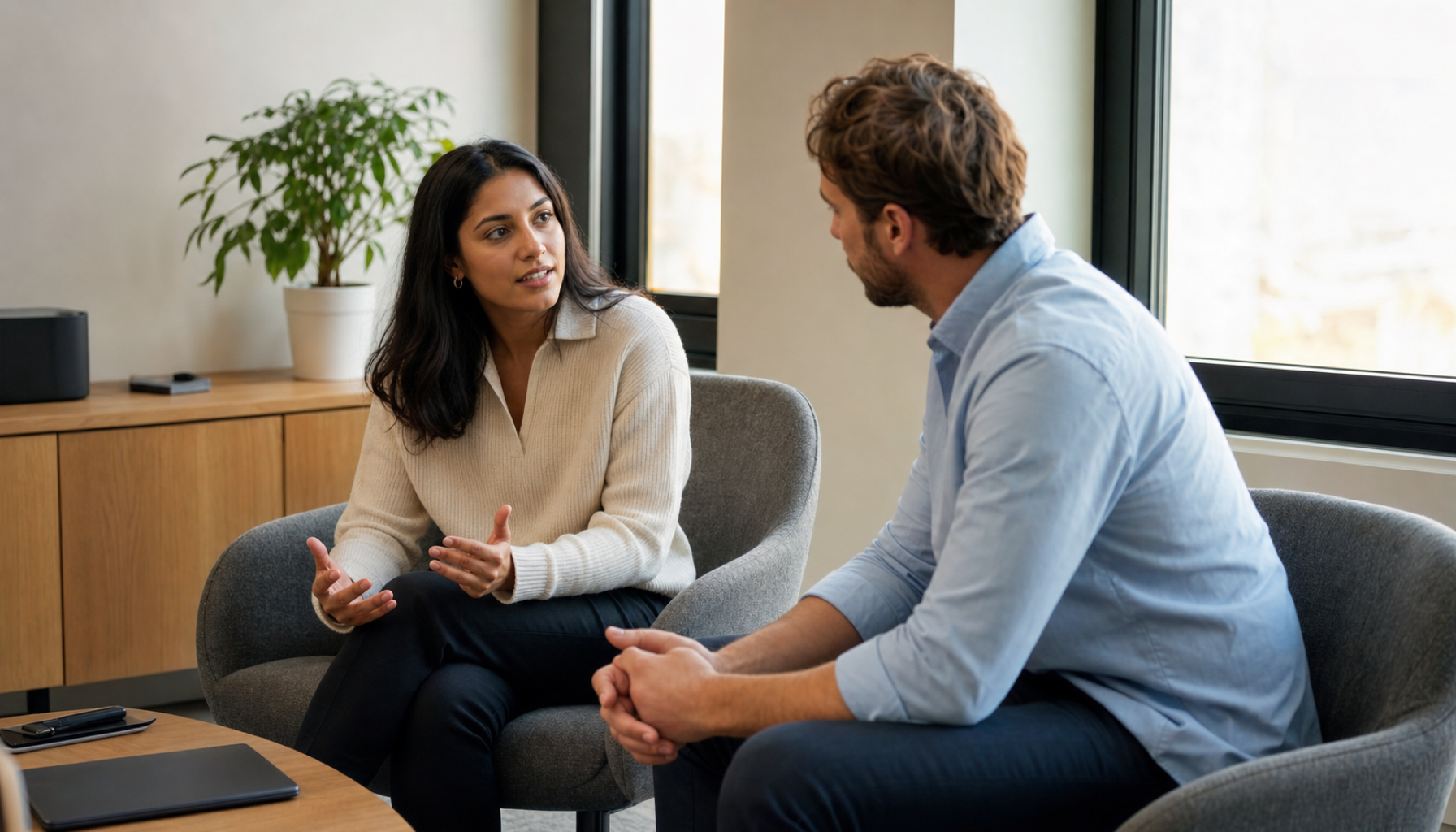 Two colleagues in a calm one-to-one conversation in a quiet corner of an office, one listening attentively while the other speaks, soft natural light, smart-casual dress.