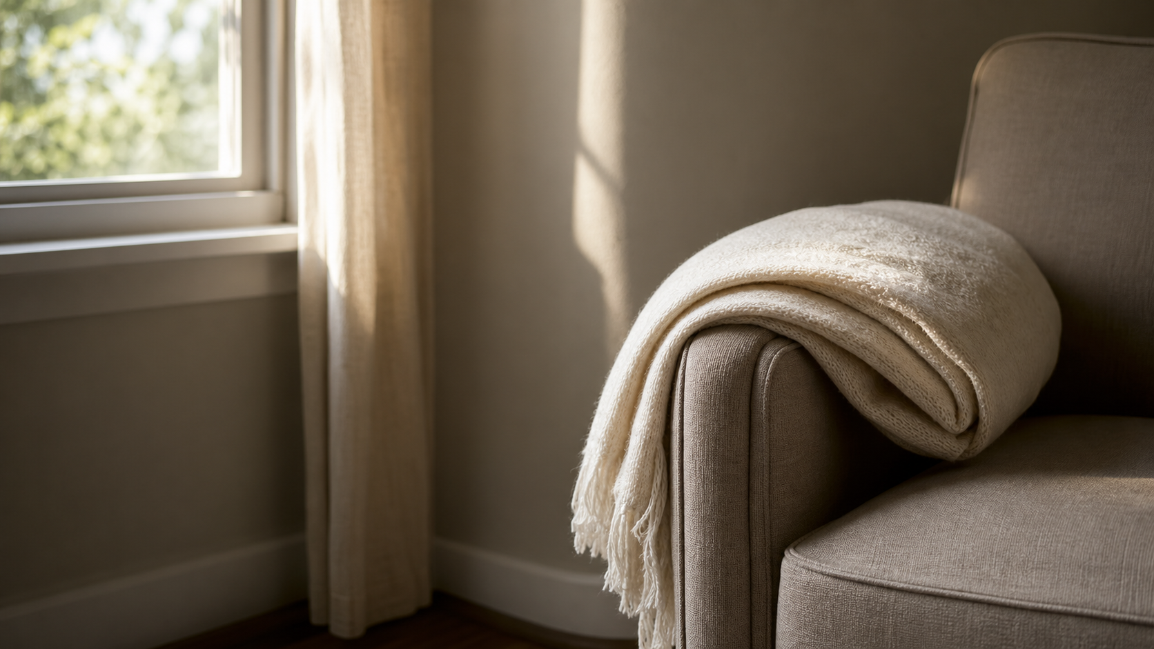 A softly lit corner with a comfortable upholstered chair and a folded cream throw on the arm in soft afternoon window light