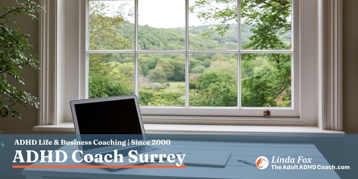 A calm home study desk beside a Georgian sash window looking out onto rolling green Surrey countryside in soft morning light